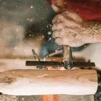 Close-up of a craftsman's hands working on the shape of a piece of light wood